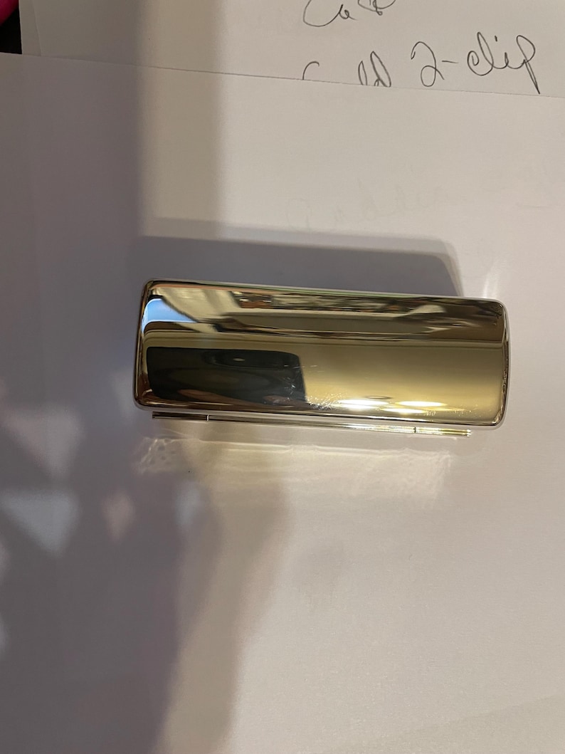 May include: A silver metal cigarette case with a hinged lid.