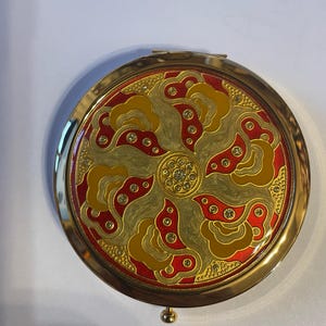 Estojo de pó compacto redondo retrô Art Déco dourado/vermelho com espelho e fecho de botão de pressão à moda antiga.