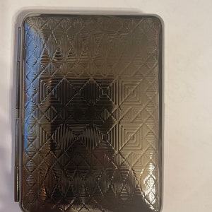 May include: A silver cigarette case with a geometric pattern embossed on the front.