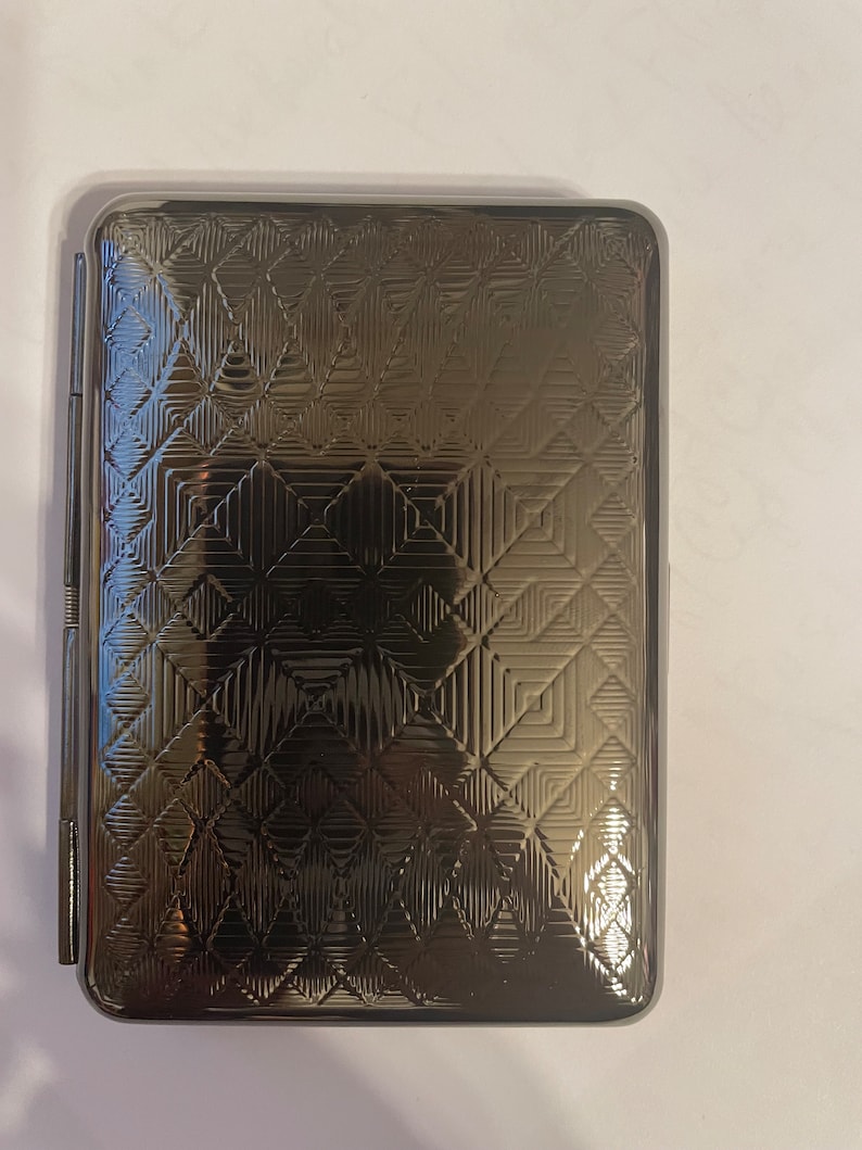 May include: A silver cigarette case with a geometric pattern embossed on the front.
