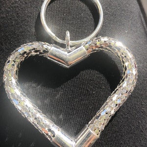 May include: A silver heart-shaped keychain with a silver ring attached. The heart is made of a chain-link design.