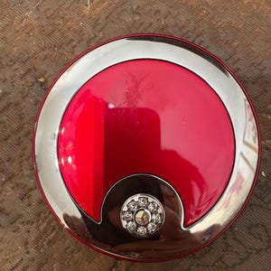 May include: A red compact mirror with a silver rim and a decorative crystal design in the center.