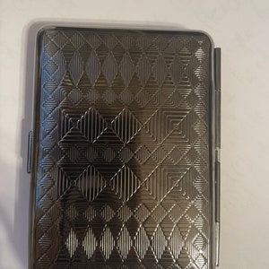 May include: A silver cigarette case with a geometric pattern.