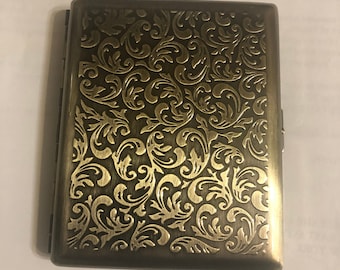 May include: A gold metal cigarette case with an ornate, embossed floral design.