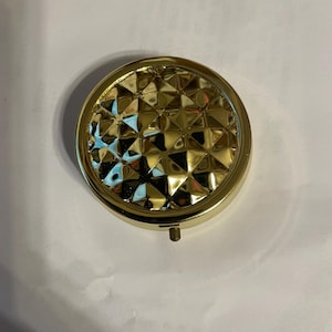 May include: A gold round compact with a diamond pattern on the lid.