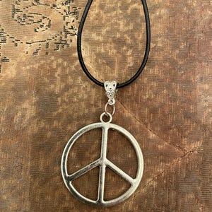 Può includere: Una collana con un ciondolo a forma di segno della pace argentato su un cordoncino in pelle nera.