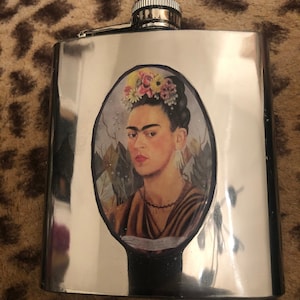 May include: A silver flask with a colorful image of Frida Kahlo wearing a flower crown.