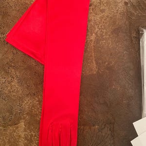 May include: A pair of long, red satin gloves. The gloves are folded in half and the fingertips are visible.