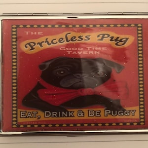 May include: A red and gold compact mirror with a black pug wearing a red bow tie. The mirror has the text "The Priceless Pug Good Time Tavern Eat, Drink & Be Puggy" on it.