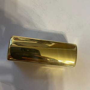 May include: A gold-colored rectangular box with a smooth, shiny surface.