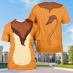 Può includere: T-shirt arancioni con un disegno di leone. La parte anteriore della maglietta presenta una criniera e un petto di leone, mentre il retro mostra una coda. Il disegno è stampato su una t-shirt a maniche corte.