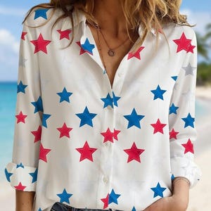 May include: White button-down shirt with a pattern of red, blue, and gray stars. The long-sleeved shirt has a collared neckline and is paired with blue jeans. The shirt's design is patriotic and eye-catching.