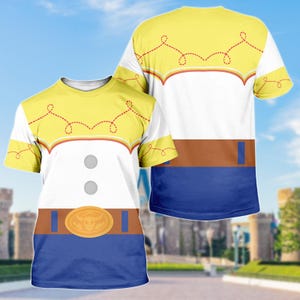 May include: A white t-shirt with a yellow yoke and sleeves, featuring a brown belt design with a gold buckle and blue bottom. The shirt has two gray buttons and a decorative red stitch pattern. The design is reminiscent of a cowgirl costume.