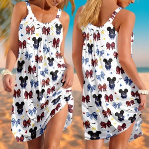 Puede incluir: Vestido blanco sin mangas con un estampado de lazos rojos, azules y negros, siluetas de Mickey Mouse y pequeñas estrellas. El vestido tiene un escote fruncido y una abertura lateral, perfecto para la playa o uso casual.
