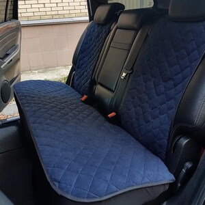 May include: Blue quilted car seat covers installed in the back seat of a black SUV. The covers are designed to protect the seats from dirt, spills, and pet hair.