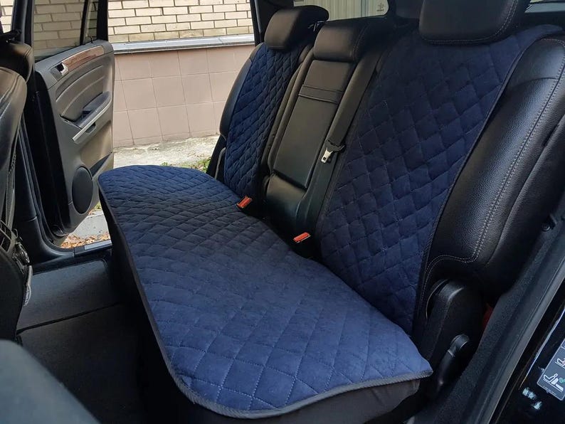 May include: Blue quilted car seat covers installed in the back seat of a black SUV. The covers are designed to protect the seats from dirt, spills, and pet hair.
