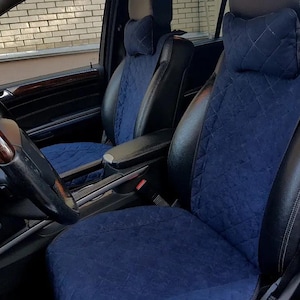 May include: Two car seats with blue quilted covers and black leather accents. The seats are installed in a car with a brown leather steering wheel.