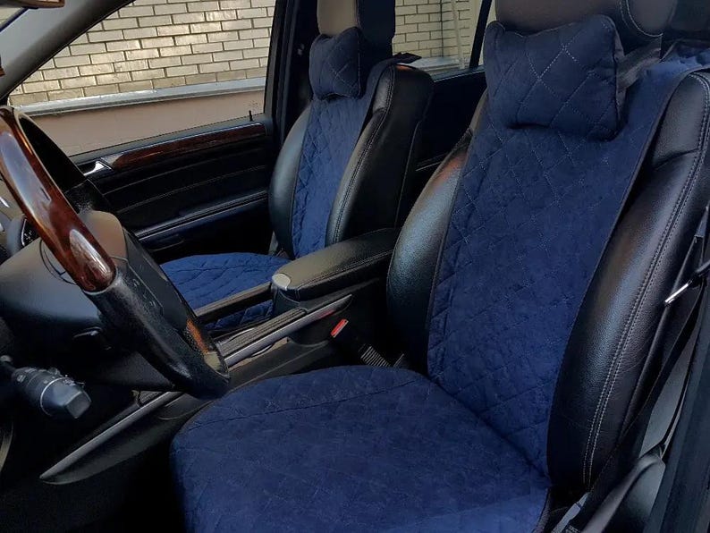May include: Two car seats with blue quilted covers and black leather accents. The seats are installed in a car with a brown leather steering wheel.