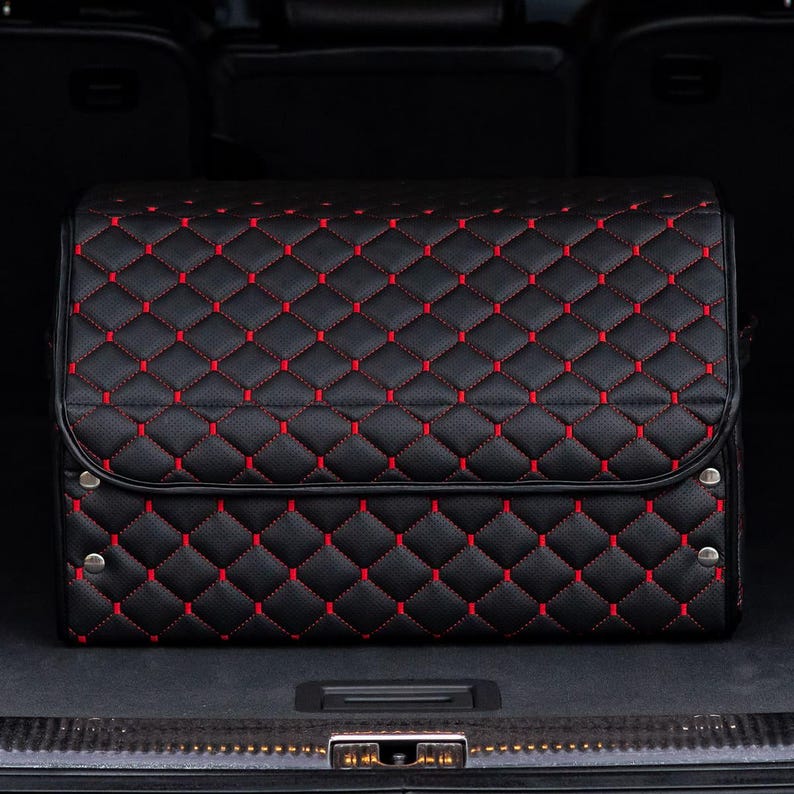 May include: Black quilted storage box with red stitching. The box is in the trunk of a car.