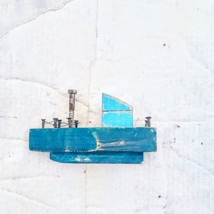 Pu&ograve; includere: Una piccola barca di legno con uno scafo blu e una vela blu chiaro. La barca &egrave; decorata con viti e chiodi arrugginiti.