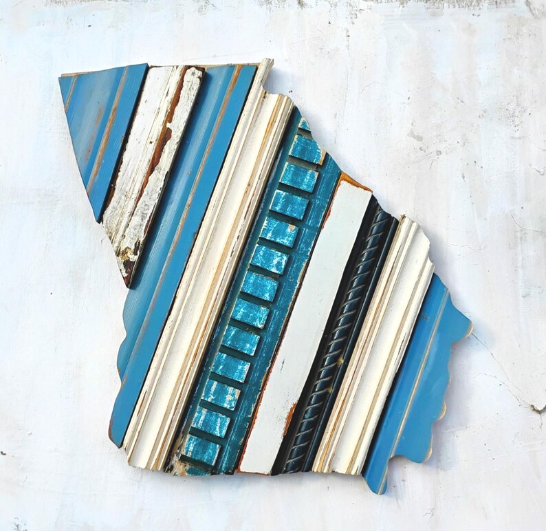 May include: A blue, white, and black wood wall art piece in the shape of the state of South Carolina. The wood is arranged in a diagonal pattern.