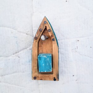 Pu&ograve; includere: Una barca giocattolo di legno con uno scafo blu-verde e un ponte in legno. La barca ha un piccolo blocco di legno all'interno ed &egrave; decorata con chiodi di metallo.