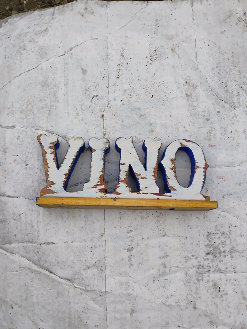 May include: White wooden sign with the word "VINO" painted in blue letters. The sign is on a white background.