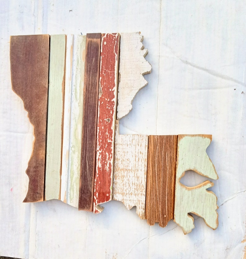 May include: A wooden wall art piece shaped like the state of Louisiana. The wood is painted in various shades of brown, white, and red, giving it a rustic and vintage look.