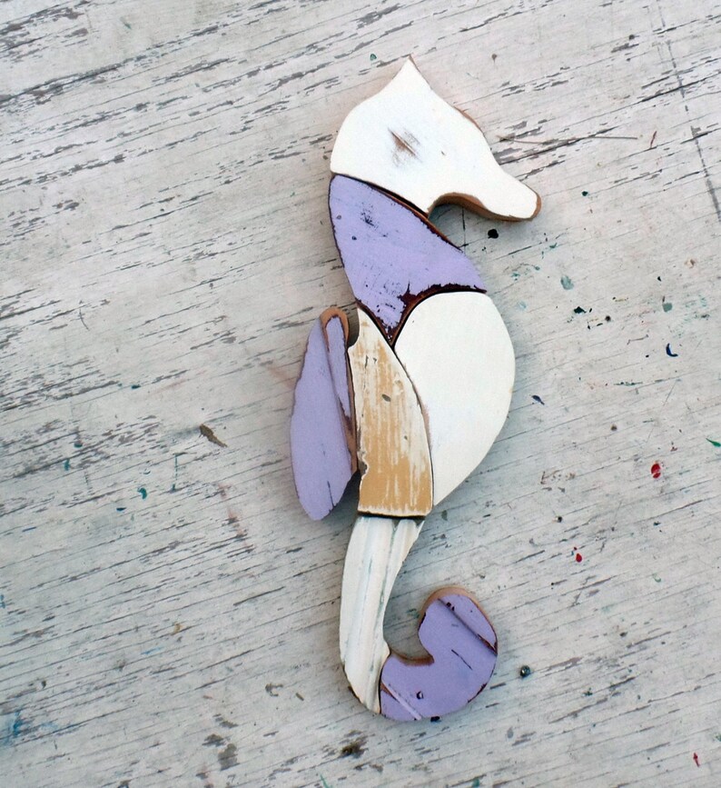 May include: A wooden seahorse sculpture painted in shades of white, purple, and brown. The seahorse is made of multiple pieces of wood that have been joined together to create a unique and whimsical design.