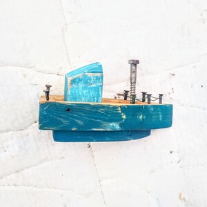 Pu&ograve; includere: Una piccola barca di legno blu giocattolo con una vite di metallo e chiodi per il dettaglio. La barca &egrave; dipinta di un colore blu chiaro e ha un aspetto invecchiato.