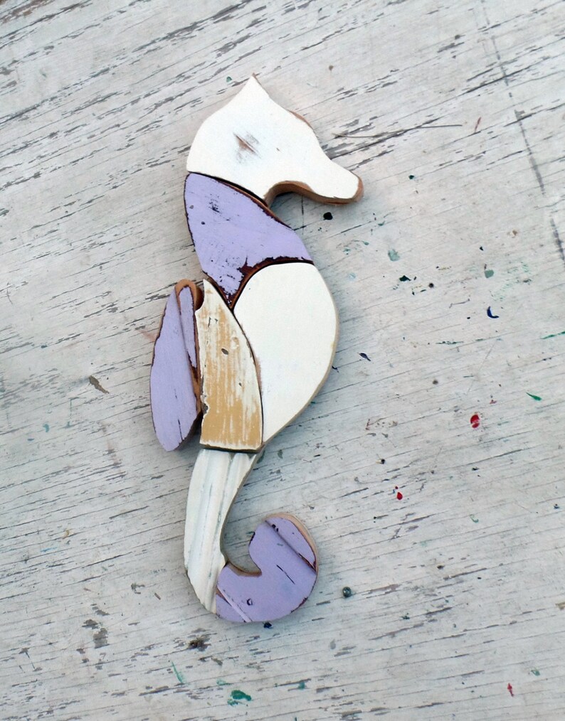 May include: A wooden seahorse sculpture painted in shades of white, purple, and yellow. The seahorse is made of multiple pieces of wood that have been joined together.