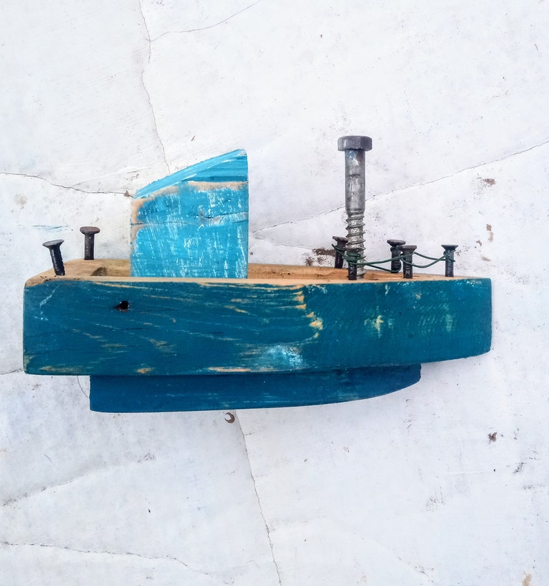 Pu&ograve; includere: Una piccola barca di legno dipinta di blu-verde con una cabina in legno blu e bianca. La barca ha una vite di metallo per l'albero maestro e diversi chiodi di metallo per una ringhiera.