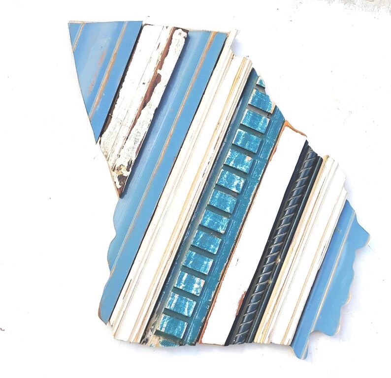 May include: A blue, white, and teal wood wall art piece in the shape of the state of Georgia. The wood is arranged in a diagonal pattern, creating a unique and modern look.
