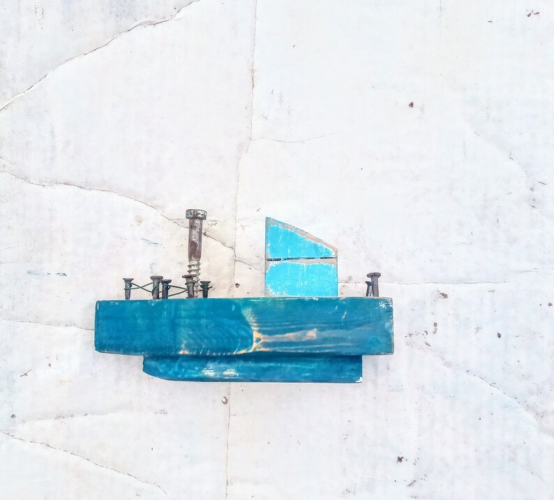 Pu&ograve; includere: Una piccola barca di legno con uno scafo blu e una vela blu chiaro. La barca &egrave; decorata con viti e chiodi arrugginiti.