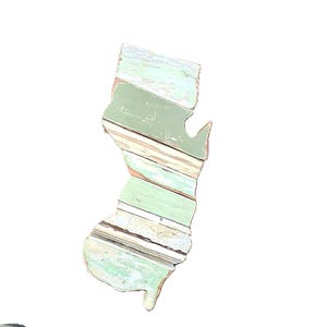 May include: Wooden wall art in the shape of New Jersey. The artwork is made of distressed wood planks in shades of green, white, and brown. The state outline is visible against a white background.