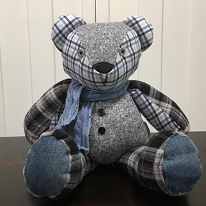 May include: A gray, blue, and black patchwork teddy bear with a blue scarf. The bear has button eyes and a black nose.