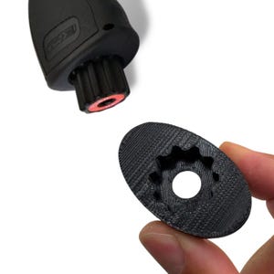 May include: Black, 3D-printed tool parts. One part is a cylindrical piece with a red ring and a gear-like design. The other is an oval-shaped piece with a gear-like hole in the center. The parts are shown against a white background.