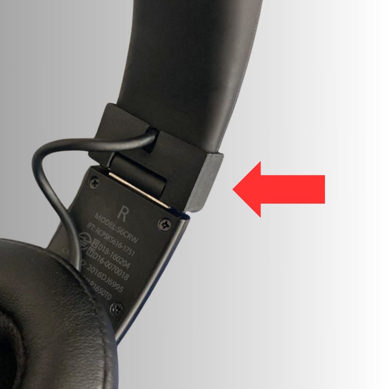May include: Close-up of black over-ear headphones. The image focuses on the hinge and the connection point of the ear cup to the headband. The text "R" is visible, along with model and certification information.