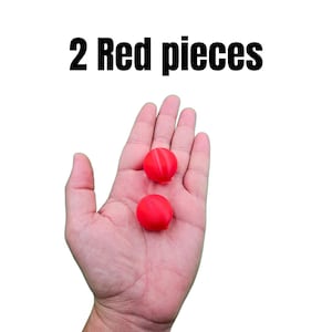 May include: Two small, bright red spherical objects are held in an open hand against a white background. The text "2 Red pieces" is displayed above the hand in bold black letters.
