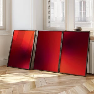 Peut inclure: Trois impressions d'art abstrait encadrées avec un dégradé de couleurs rouge et rouge foncé. Les cadres sont noirs et les impressions sont accrochées à un mur blanc.