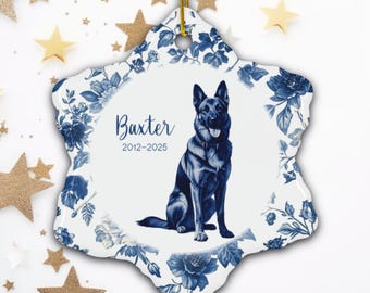 May include: A white ceramic ornament with a blue floral design and a German Shepherd illustration. The ornament has the name "Baxter" and the years "2012-2025" printed on it. The ornament is shaped like a six-pointed star and has a gold string for hanging.