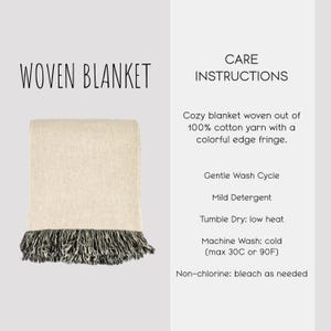 May include: A woven blanket made of 100% cotton yarn in a light beige color with a dark, multi-colored edge fringe. The text reads: WOVEN BLANKET, CARE INSTRUCTIONS, Cozy blanket woven out of 100% cotton yarn with a colorful edge fringe, Gentle Wash Cycle, Mild Detergent, Tumble Dry: low heat, Machine Wash: cold (max 30C or 90F), Non-chlorine: bleach as needed.