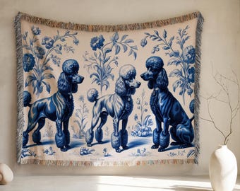 May include: A woven throw blanket featuring three stylized poodles in shades of blue against a cream background with floral patterns. The blanket has a fringed edge and is displayed on a wall.