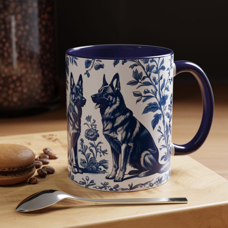 May include: A white ceramic mug with a blue rim and handle. The mug features a blue and white design of two German Shepherd dogs in a floral pattern.