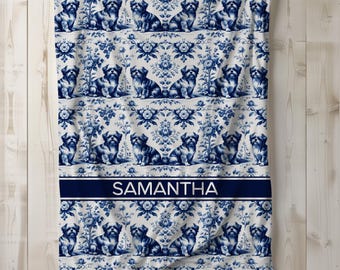 May include: A white and blue patterned blanket featuring a repeating design of Shih Tzu dogs and floral elements. The blanket has a navy blue band with the name "SAMANTHA" in white text.