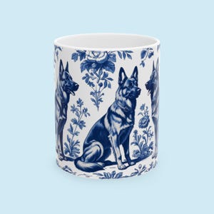 May include: A white ceramic mug with a blue and white pattern of German Shepherd dogs and floral designs. The dogs are in a sitting position and the flowers are in a variety of styles.
