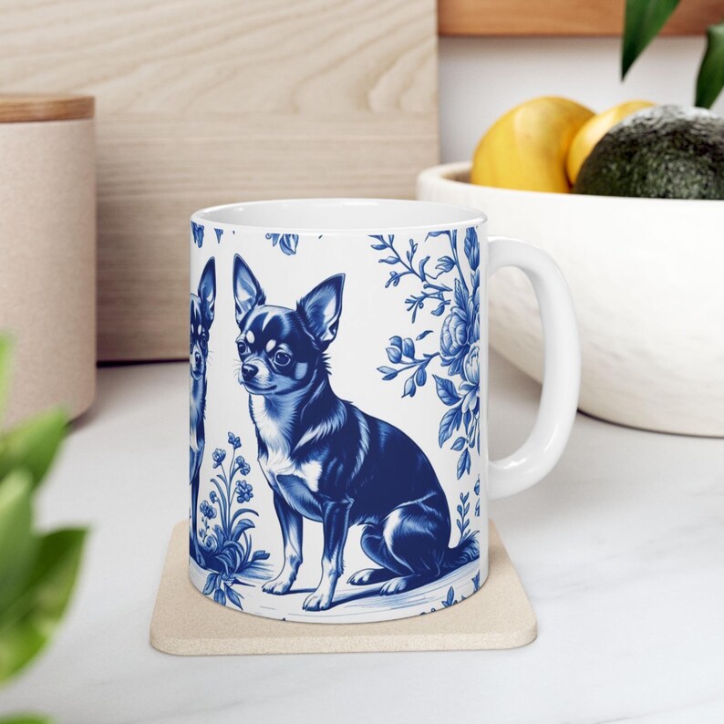 May include: White ceramic mug with a blue and white Chihuahua dog illustration and floral patterns. The mug has a handle and is on a square coaster. The design is reminiscent of traditional blue and white china.