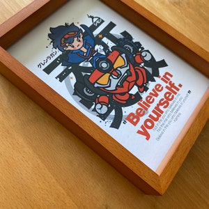 K&ouml;nnte beinhalten: Ein gerahmter Druck mit einer Cartoon-Illustration einer Figur in einem roten und gelben Roboter. Der Druck hat einen wei&szlig;en Hintergrund mit schwarzem Text, der lautet: "Glaube an dich selbst. Nicht an das Ich, das an dich glaubt. Nicht an das Du, das an mich glaubt. Glaube an das Du, das an dich selbst glaubt" - Kamina.