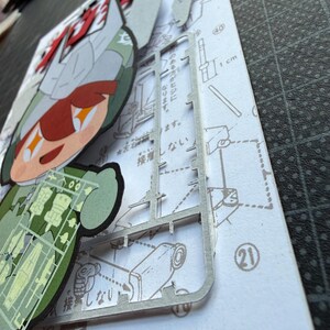May include: A partially assembled model kit featuring a cartoon character with red and green accents. The kit includes a sprue of plastic parts and a printed instruction sheet with Japanese text and diagrams. A 1 cm ruler is visible.