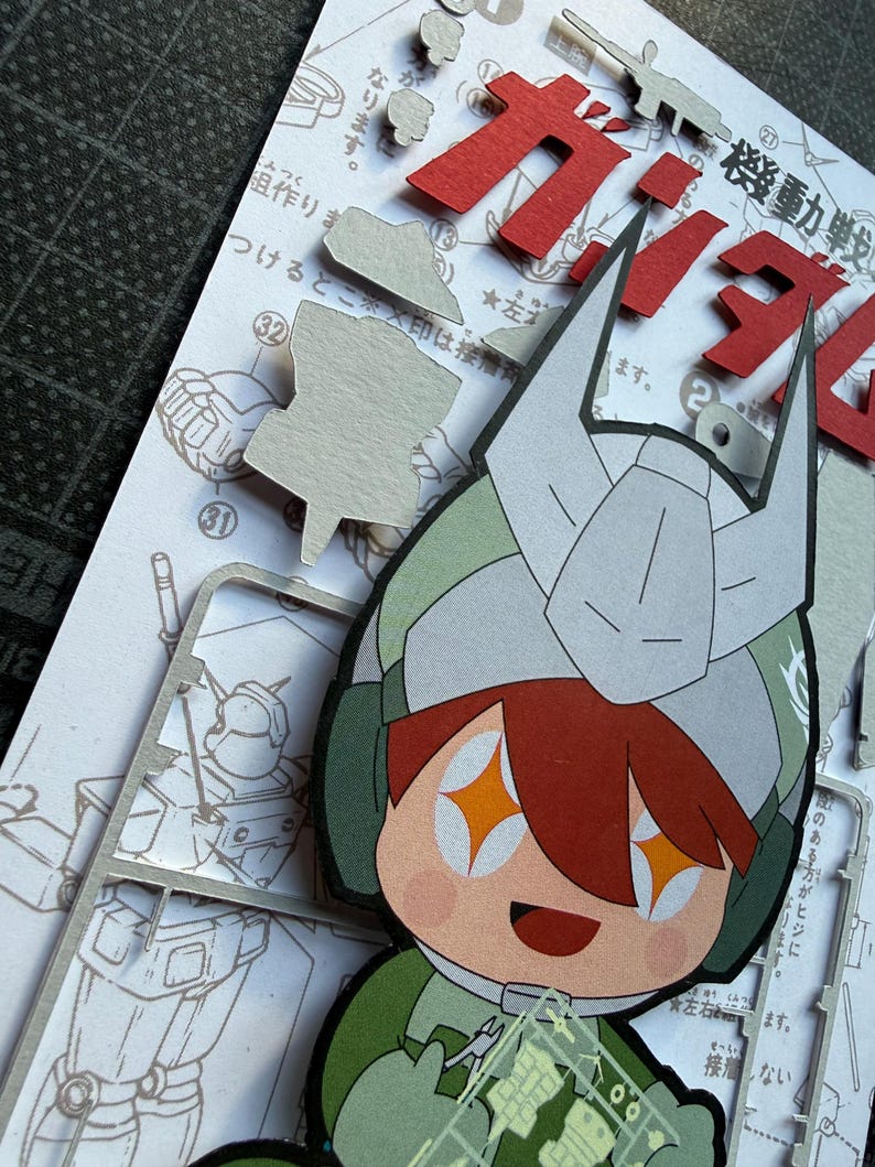 May include: A colorful paper cutout of a cartoon character wearing a helmet, with orange star-shaped eyes and a smiling expression. The character is holding a clear plastic sheet with small parts. Japanese text and cut-out pieces are visible.